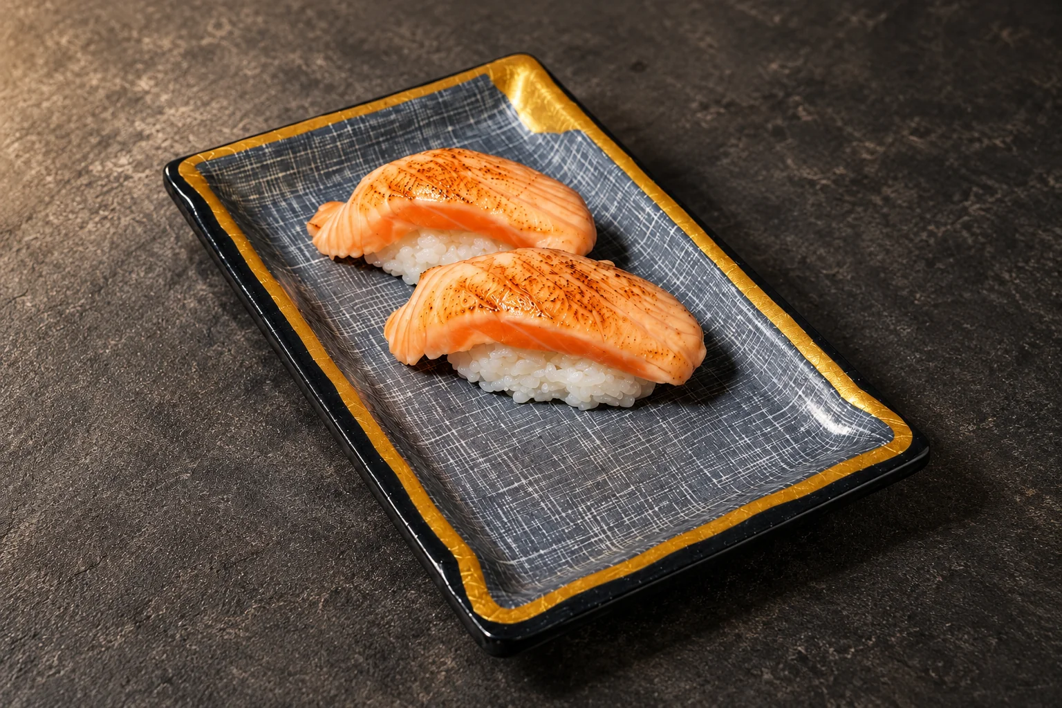 Deux nigiris de saumon flambé sur une assiette rectangulaire bleu-gris à liseré doré.